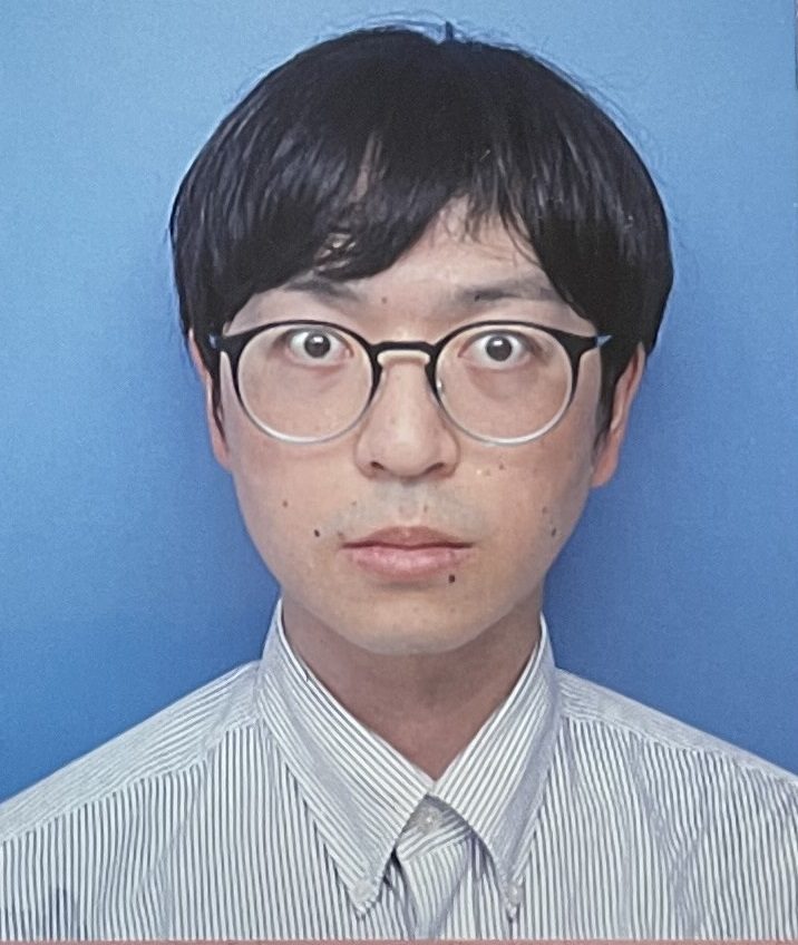 眼鏡をかけた男性が青い背景の前で真剣な表情をしているポートレート。