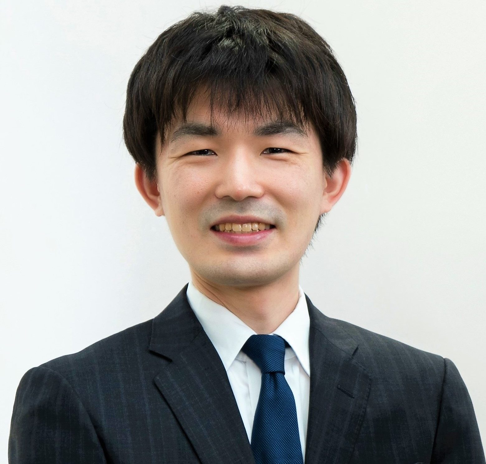 稲永亮平氏がスーツを着て微笑んでいるポートレート。背景は白色でシンプル。