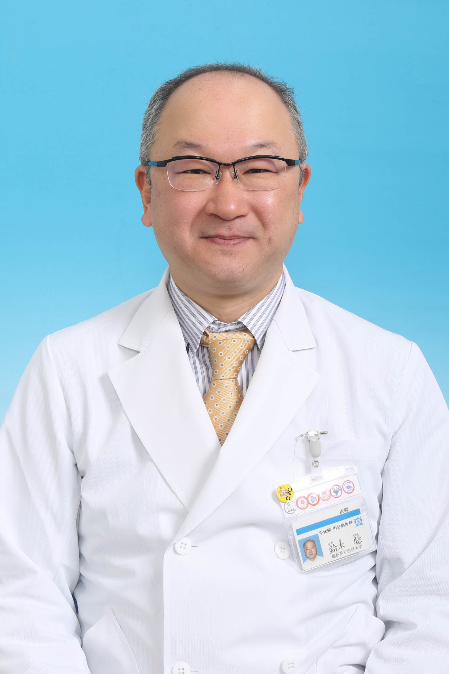 医療白衣を着た男性が微笑んでいるポートレート。背景は青色で、福島県立医科大学に関連する可能性がある。