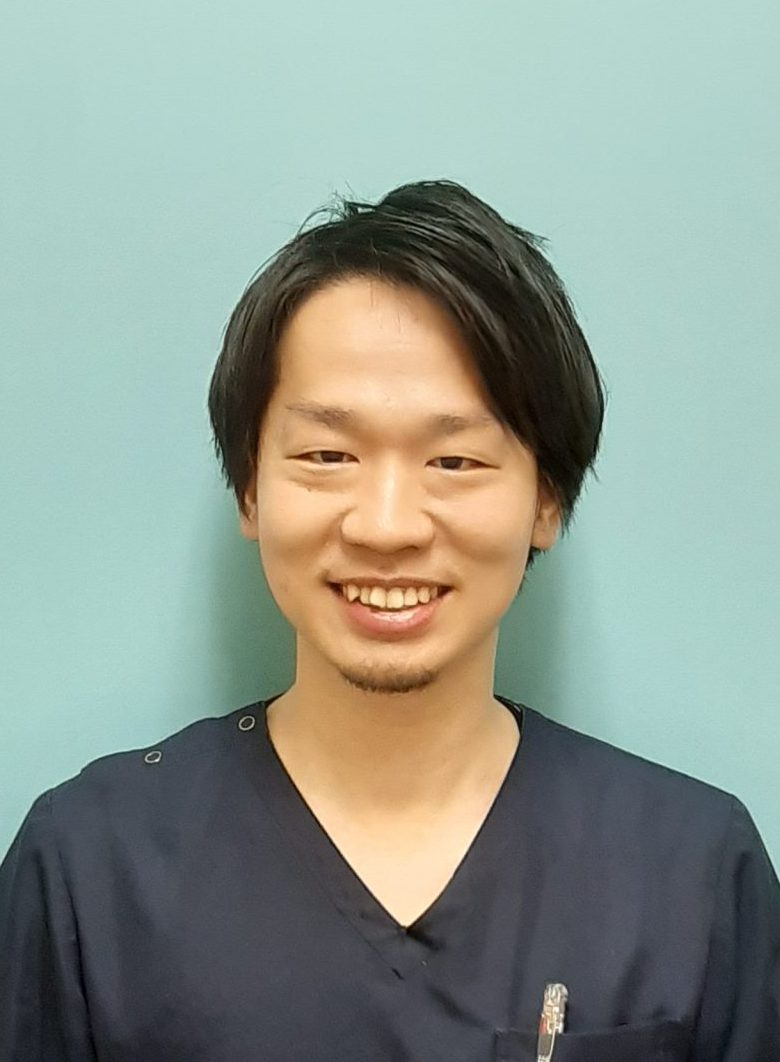 医療現場での服装をした男性が微笑んでいるポートレート。背景は淡い青色。
