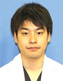 西浦司人さんの医療用白衣を着た肖像写真。背景は青色。