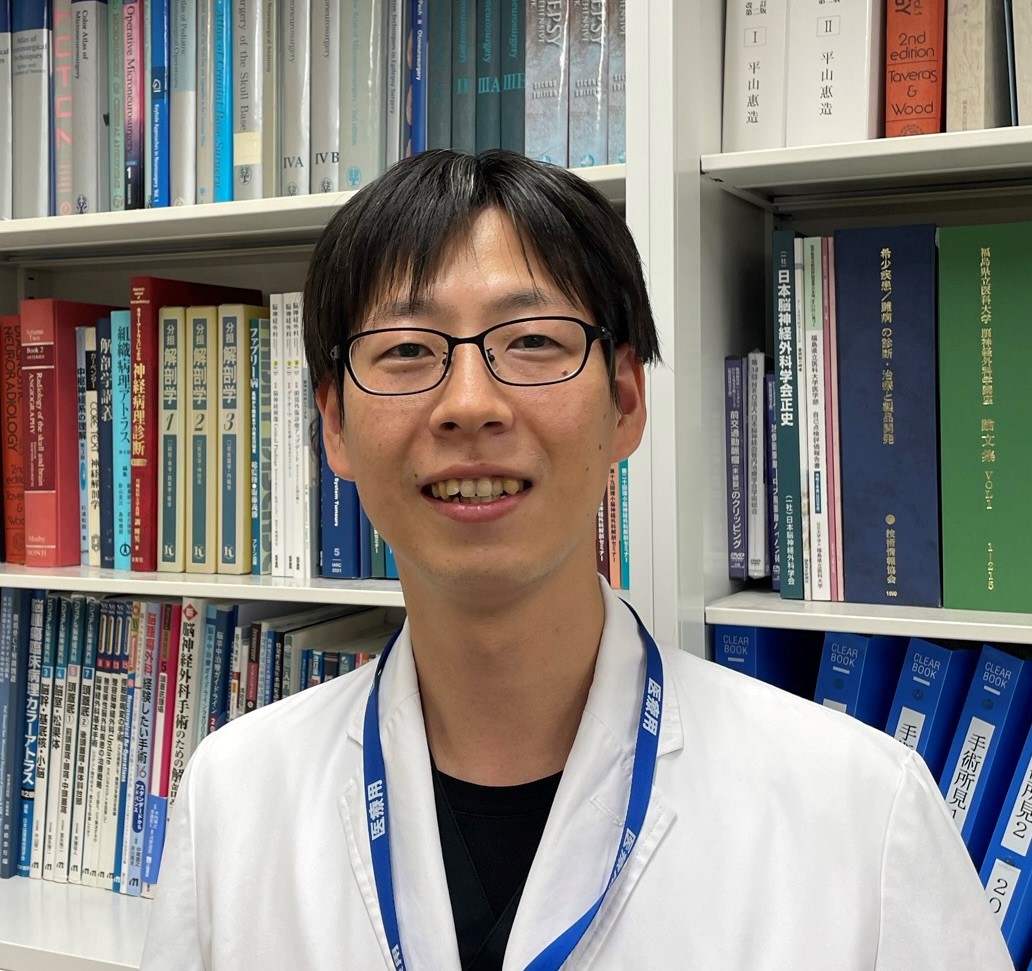 長井健一郎助手が医学部の書棚の前で微笑んでいる写真。