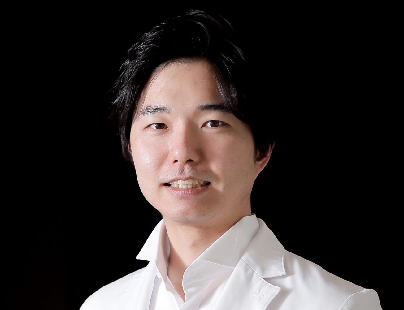 福島県立医科大学の医師が白衣を着て微笑んでいるポートレート。背景は黒。