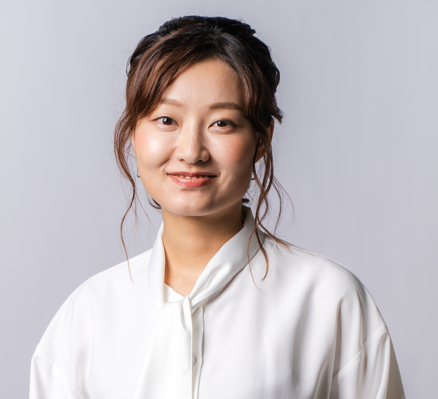 白いシャツを着た女性が微笑んでいるポートレート。背景は淡いグレー。