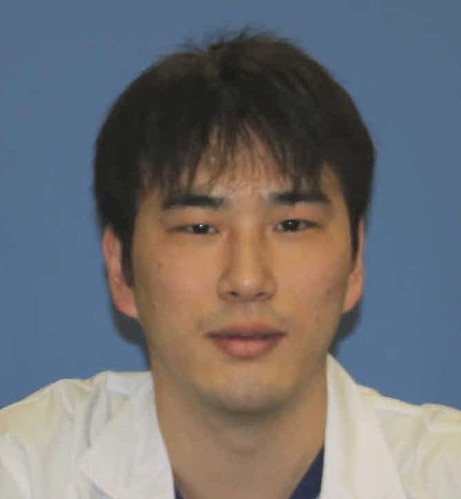 大学院生の丸山裕也さんが白衣を着て微笑んでいるポートレート。背景は青色。