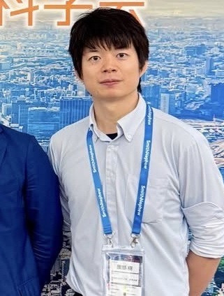 園部樹助教がネームプレートを首から下げてまじめな表情をしているポートレート。